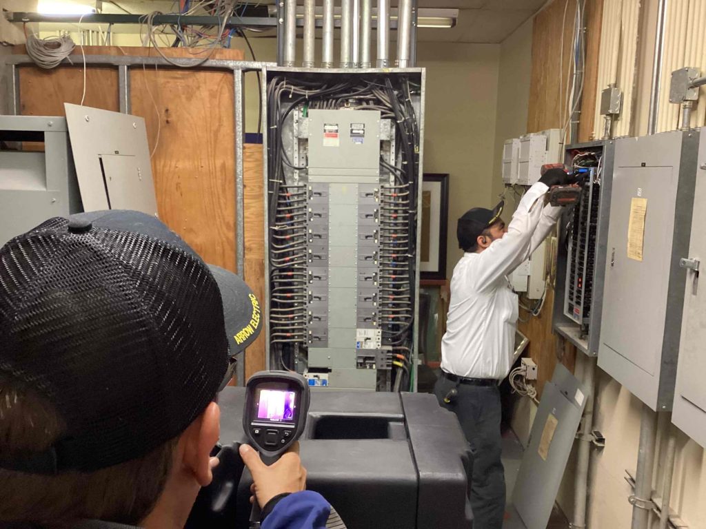 An Arrow Electric technician being monitored with a thermal imaging camera while working on an electrical panel.