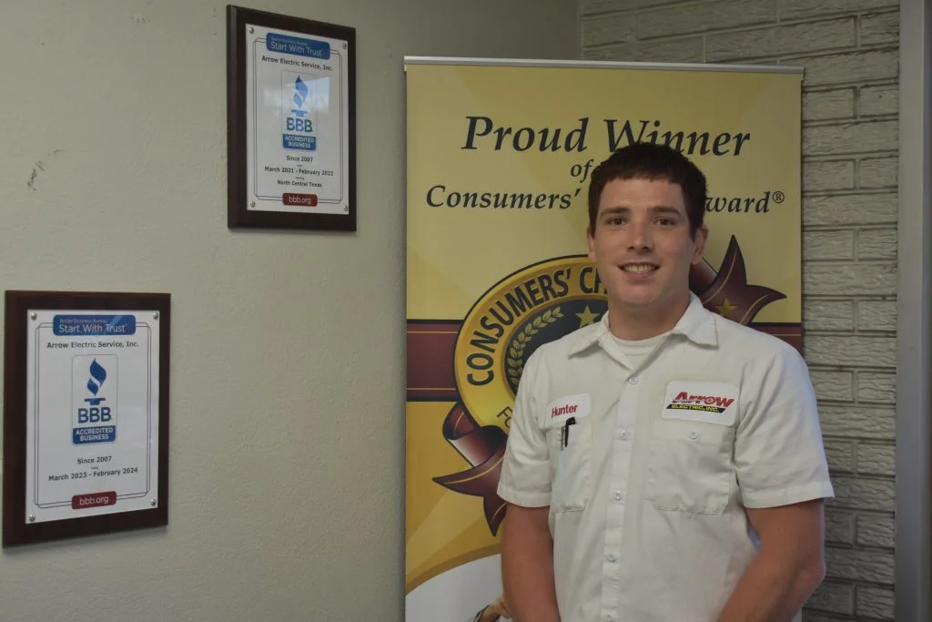 Employee Hunter from Arrow Electric standing in front of the company's achievement awards